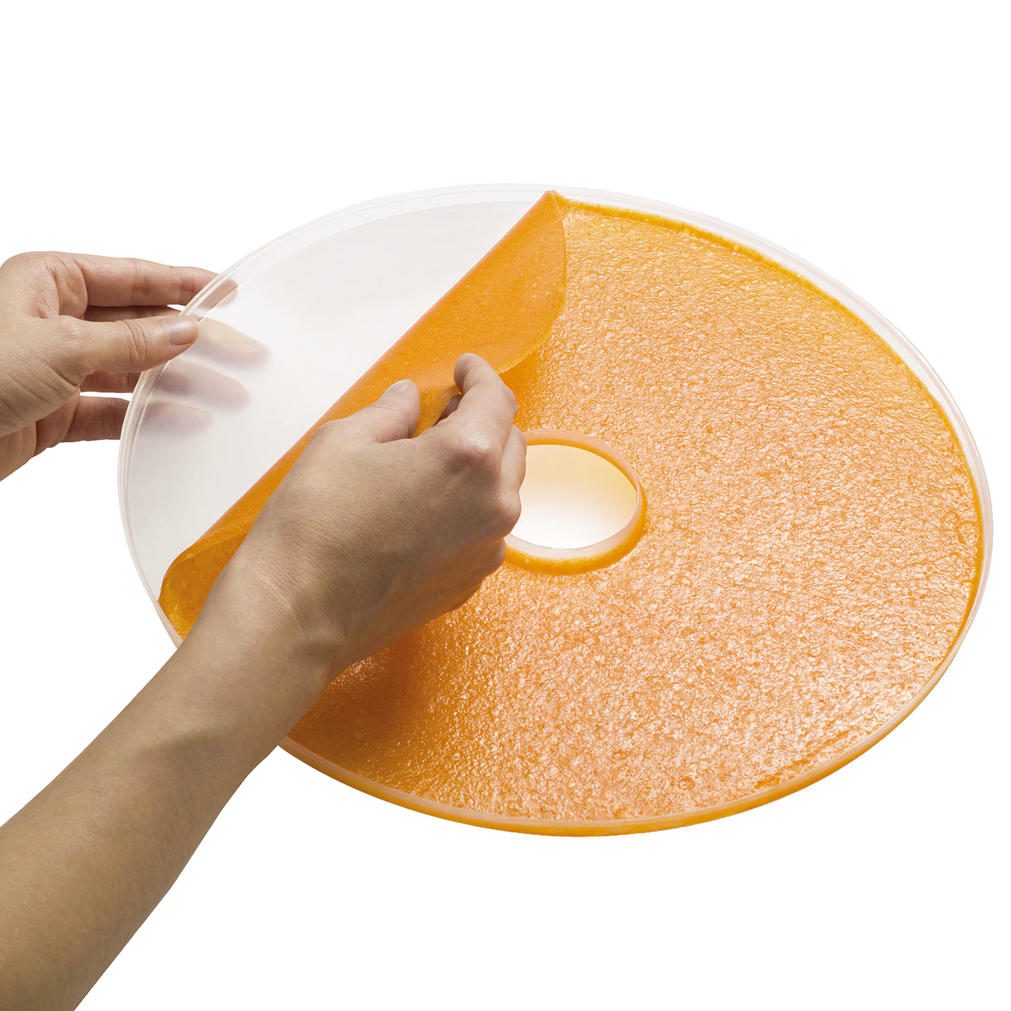 Hands peeling homemade orange fruit leather from a flexible round sheet designed to fit Presto dehydrator trays, featured in Kitchen & Food and Food Preservation collections.