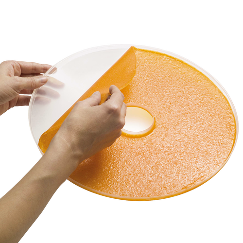 Hands peeling homemade orange fruit leather from a flexible round sheet designed to fit Presto dehydrator trays, featured in Kitchen & Food and Food Preservation collections.