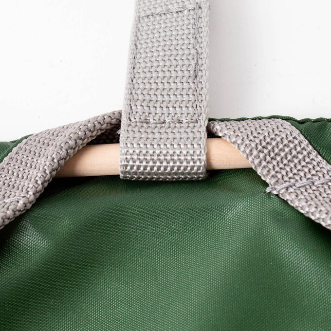 Close-up of a green Amish clothespin bag featuring a sturdy gray strap with reinforced stitching clipped over a wooden dowel, handcrafted in the USA for Home & Decor and Laundry Supplies collections.