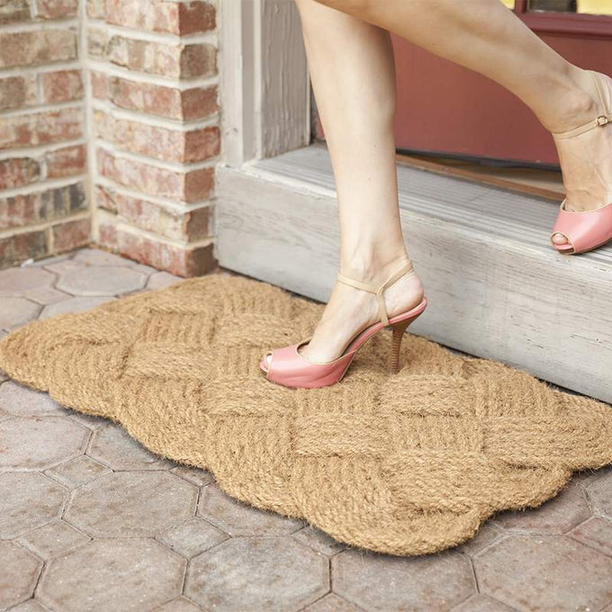 Handwoven natural coconut fiber doormat with a braided design, shown at a doorstep with a person stepping down, featured in Home & Decor, Home Textiles, and Best Sellers collections.
