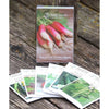 Collection of heirloom seed packets arranged on weathered wood with a compact box featuring vibrant radishes; part of Farm, Garden & Tool and USA Made selections.