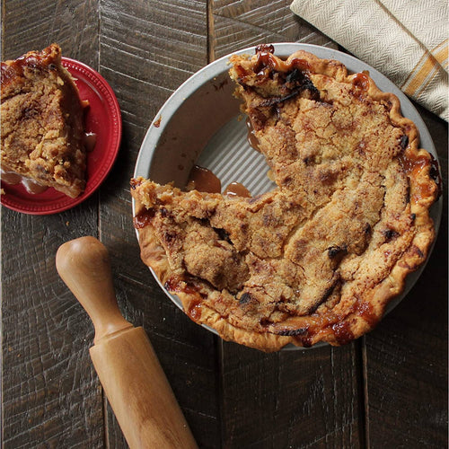 Freshly baked pie with a golden crumb topping in a 9-inch aluminized steel pan, set on a rustic wooden table with a rolling pin and a slice served on a red plate, ideal for Kitchen & Food, Baking Supplies, Cookware, and USA Made collections.