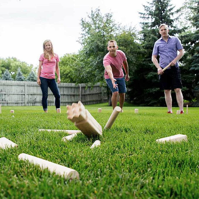 Three people enjoying a handcrafted wooden outdoor yard game on green grass with wooden dowels and blocks scattered, perfect for Toys, Books & Games and Lawn Games collections.