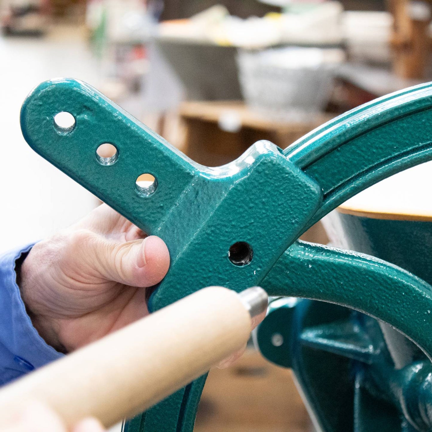 Close-up of a person attaching a durable green metal handle extension with multiple mounting holes to a grain mill crank, designed to improve leverage for easier grinding in Kitchen & Food, Grain Mills, Best Sellers, and Bread Making Supplies collections.