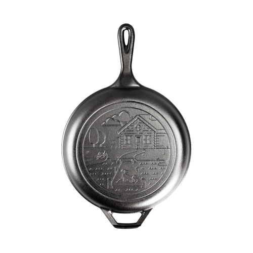 Black cast iron frying pan with handle, featuring an embossed cozy cabin scene on the cooking surface, ideal for camping, kitchen, and cookware collections emphasizing USA made quality.