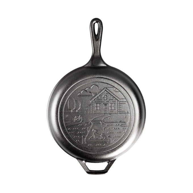 Black cast iron frying pan with handle, featuring an embossed cozy cabin scene on the cooking surface, ideal for camping, kitchen, and cookware collections emphasizing USA made quality.