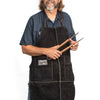 Man wearing an adjustable black leather grill apron holding wooden-handled barbecue tongs, suitable for Kitchen & Food, Grilling, and Kitchen Textiles collections.