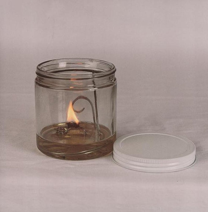 Handcrafted clear glass olive oil lamp burning with a bright flat wick inside a 16 oz jar, featuring a steel wick holder and white lid, ideal for Lamps & Lighting, USA Made, Oil Lamps, and Olive Oil Lamps collections.