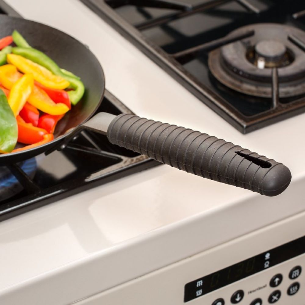 Black silicone hot handle holder securely fitted on a steel skillet handle with colorful sautéed vegetables cooking on a gas stove, ideal for kitchen gadgets and cooking helpers.