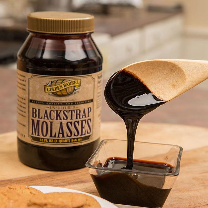 Thick, dark blackstrap molasses being poured from a wooden spoon into a small glass dish beside a 32 fl oz container, featured in Kitchen & Food, Pantry, USA Made, and Best Sellers collections.