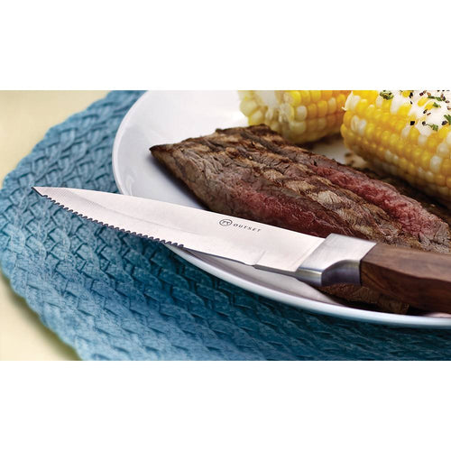 Jumbo steakhouse knife with a finely etched serrated forged stainless steel blade and polished rosewood handle resting on a plate with steak and corn, featured in Kitchen & Food and Knives & Axes collections.