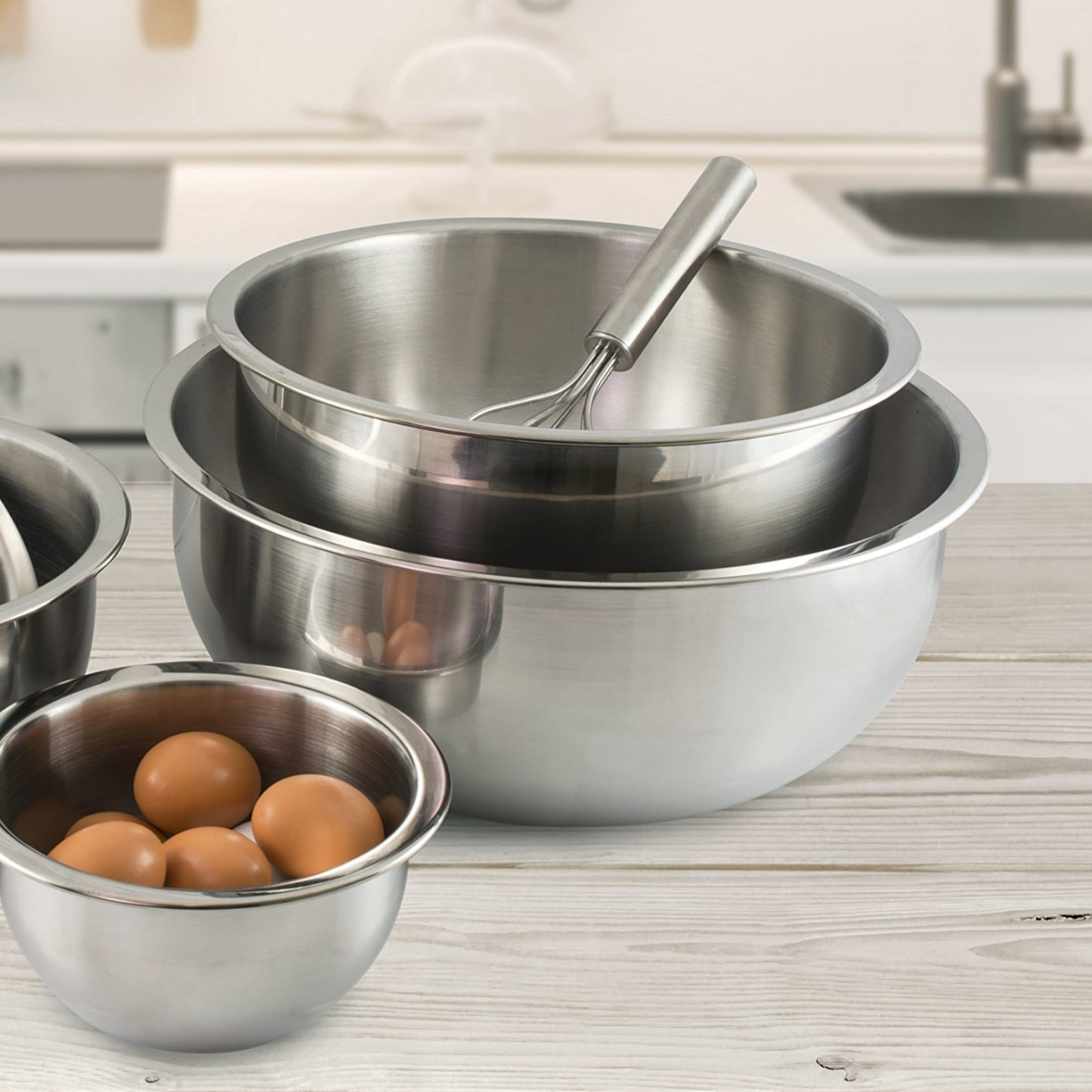 Stacked polished stainless steel mixing bowls with a whisk in the top bowl and fresh eggs in the smallest bowl, ideal for Kitchen & Food, Cookware, Baking Supplies, and Best Sellers collections.