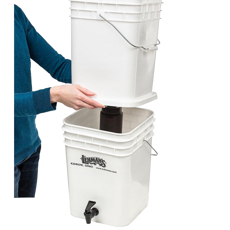 Person assembling a durable white two-bucket water filtration system with metal handles and spigot, designed for safe, large-volume water purification in farm, garden, emergency, and appliance use.