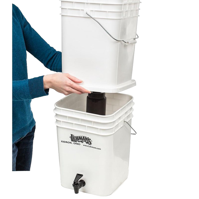 Person assembling a durable white two-bucket water filtration system with metal handles and spigot, designed for safe, large-volume water purification in farm, garden, emergency, and appliance use.