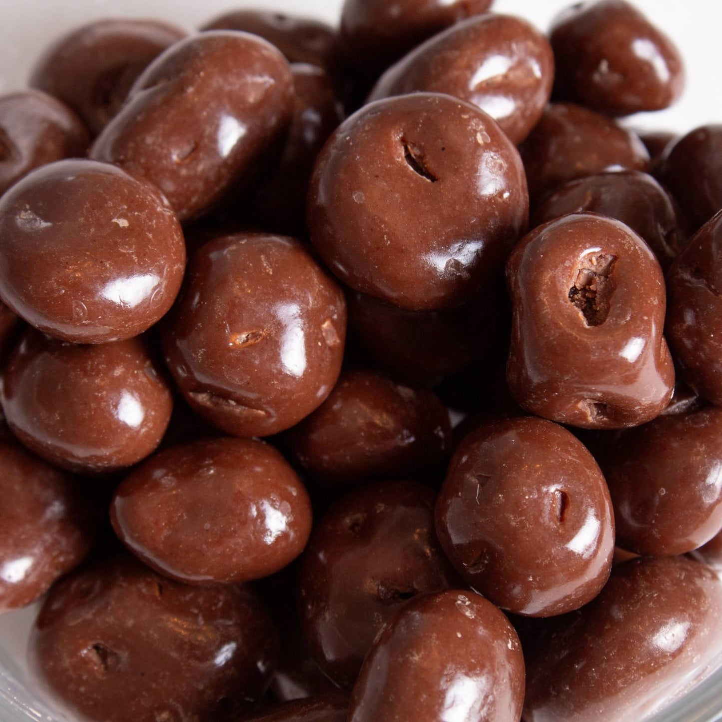 Close-up of smooth, hand-coated milk chocolate covered raisins, a handcrafted snack made in USA, perfect for Kitchen & Food, Snacks and Sweets, Candy, and Best Sellers collections.