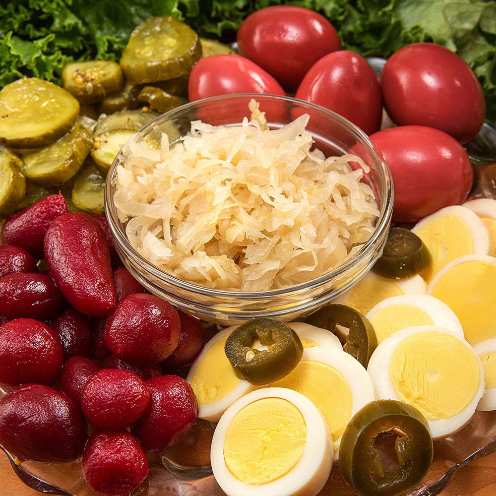 Clear glass bowl of sauerkraut surrounded by sliced hard-boiled eggs topped with jalapeño slices, red pickled eggs, kidney beans, and sliced pickles on a leafy green base, ideal for Kitchen & Food, Food, Pantry, USA Made, Best Sellers, and Promo Eligible collections.