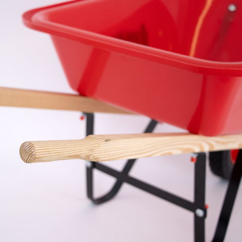 Close-up of the handcrafted hardwood handles on a bright red kids wheelbarrow designed for outdoor play in farm, garden, and lawncare activities.