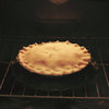 Fruit pie with a golden crust baking inside an oven, shown resting on a dark oven splatter guard with handles, suitable for Kitchen & Food, Kitchen Accessories, and Best Sellers collections.
