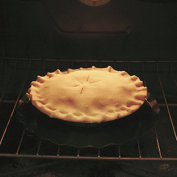 Fruit pie with a golden crust baking inside an oven, shown resting on a dark oven splatter guard with handles, suitable for Kitchen & Food, Kitchen Accessories, and Best Sellers collections.