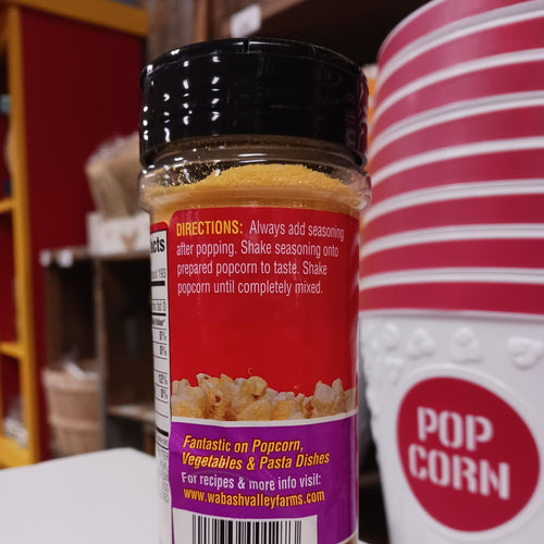 Plastic seasoning bottle with a black screw lid filled with yellow popcorn seasoning, featuring usage instructions and a colorful label, displayed near red and white striped popcorn containers, ideal for Kitchen & Food, Popcorn, USA Made, and Best Sellers collections.