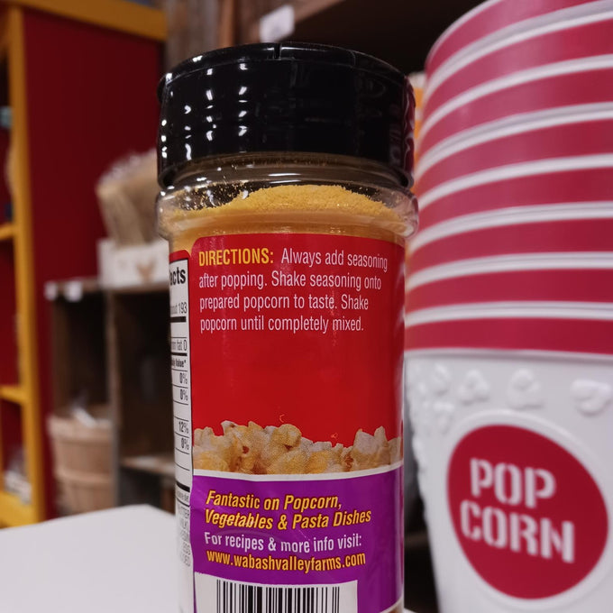 Plastic seasoning bottle with a black screw lid filled with yellow popcorn seasoning, featuring usage instructions and a colorful label, displayed near red and white striped popcorn containers, ideal for Kitchen & Food, Popcorn, USA Made, and Best Sellers collections.