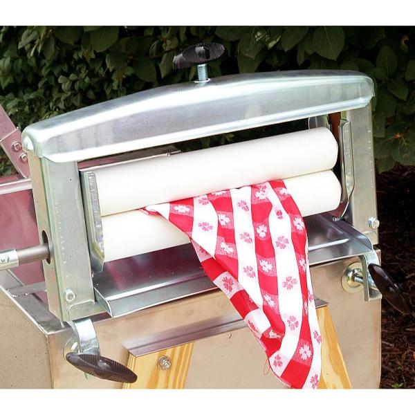 Handcrafted metal clothes wringer with white rollers gently removing water from a red and white patterned fabric, featured in Laundry Supplies and Homesteading collections.