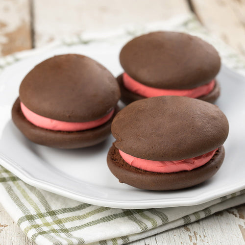 Three handcrafted chocolate whoopie pies with vibrant strawberry cream filling, arranged on a white plate over a green-striped cloth, perfect for Kitchen & Food and Snacks collections.