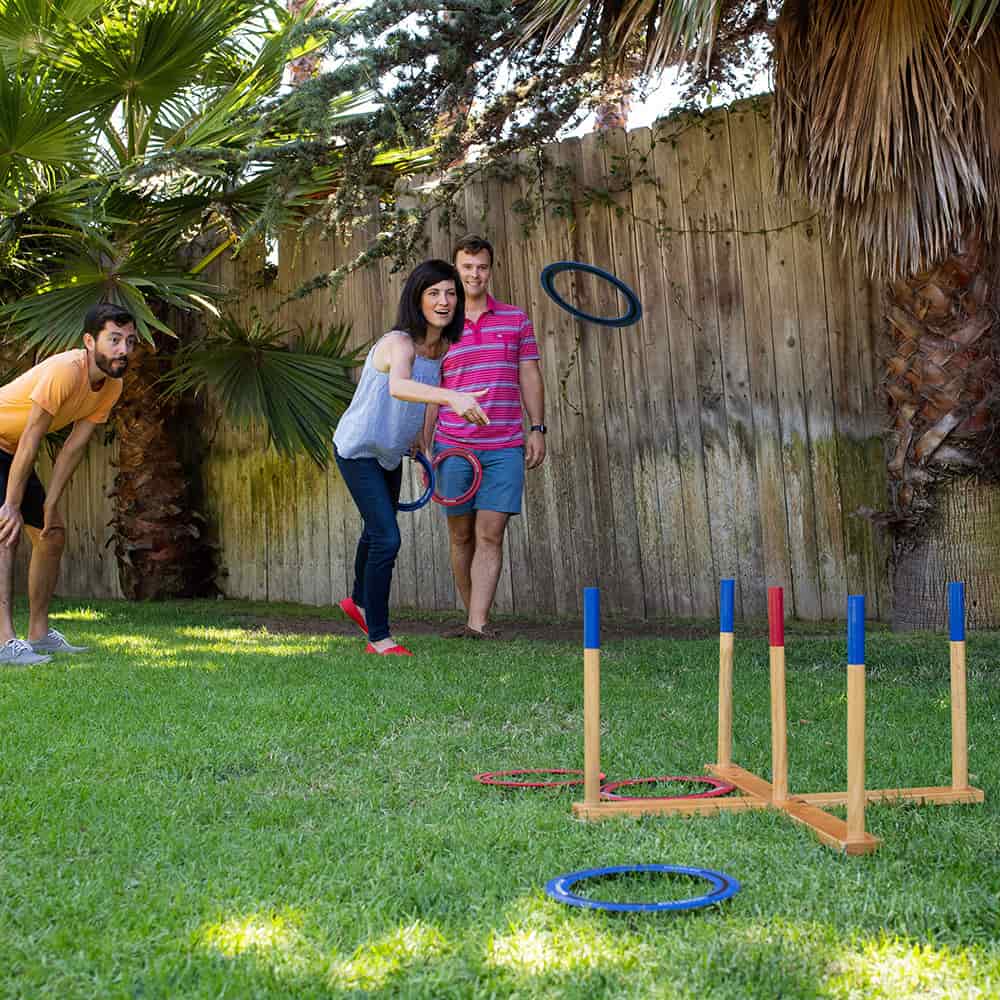 Group of three adults playing giant ring toss lawn game with wooden frame and colorful rings on a sunny backyard, included in Toys, Books & Games and Best Sellers collections