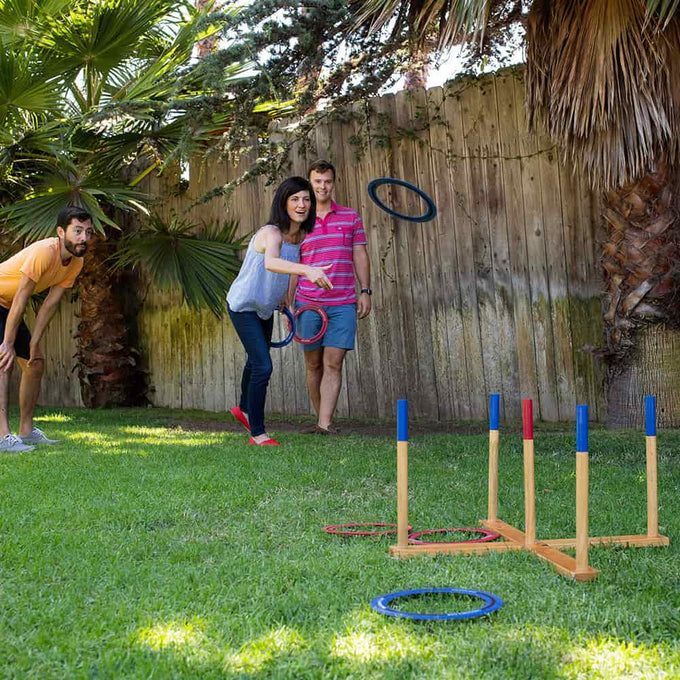 Group of three adults playing giant ring toss lawn game with wooden frame and colorful rings on a sunny backyard, included in Toys, Books & Games and Best Sellers collections