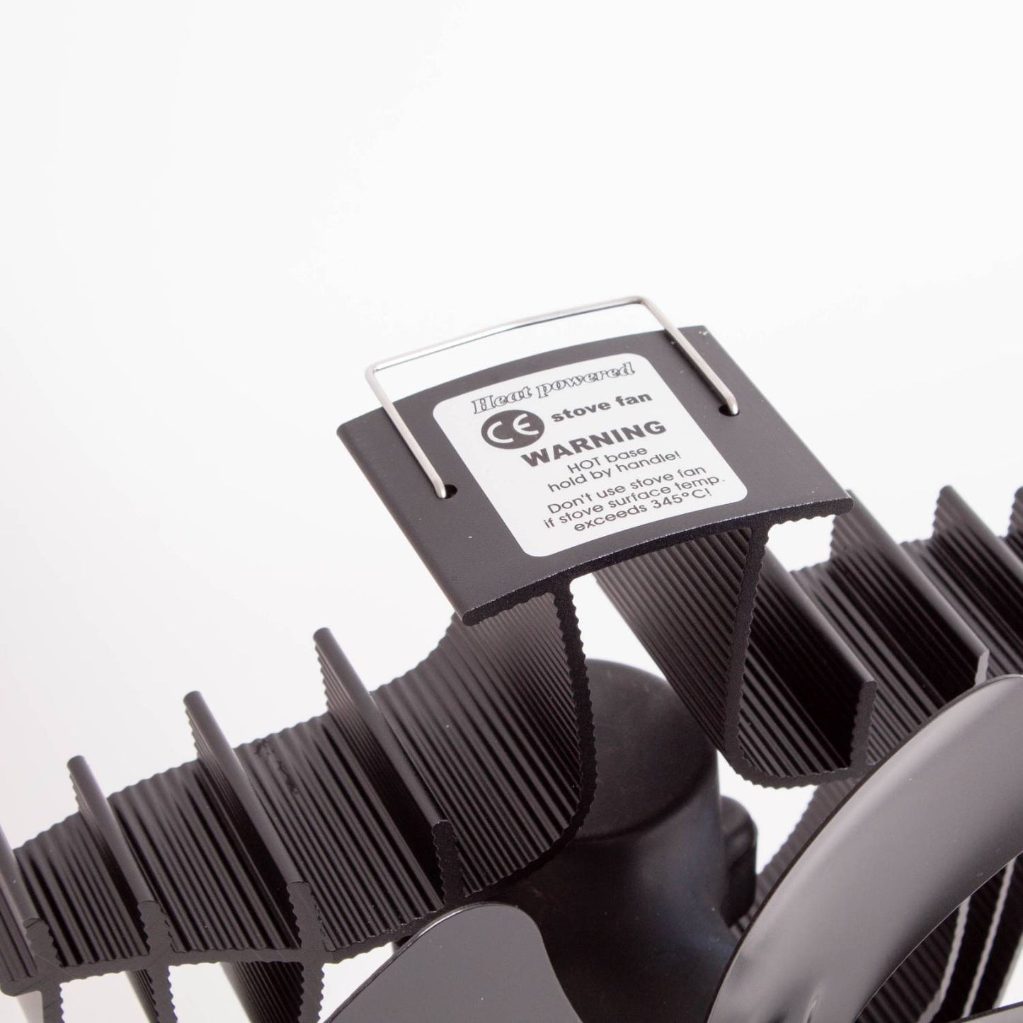 Close-up of a black heat-activated oscillating stove fan with curved finned blades and a warning label, designed to improve warm air circulation in stoves and hearth accessories collections.