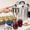 Handcrafted stainless steel funnel with clamp pouring red preserve into glass jars beside pressure canner and jar set, featured in Kitchen & Food and Food Preservation collections.