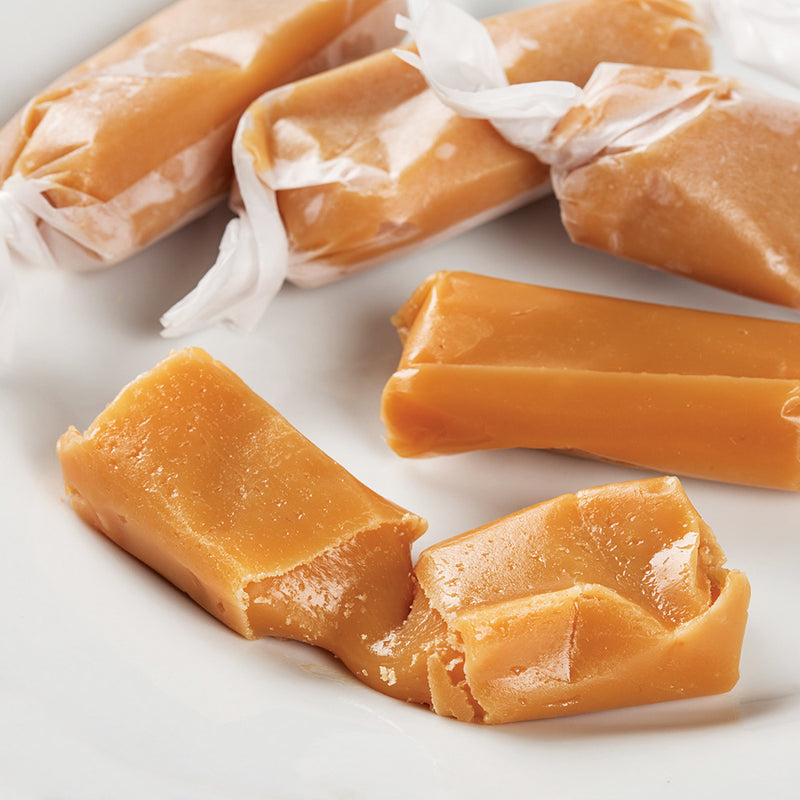 Soft, buttery caramel pieces hand wrapped in waxed paper, showcasing a homemade-style treat made in the USA, perfect for Kitchen & Food and Snacks and Sweets collections.