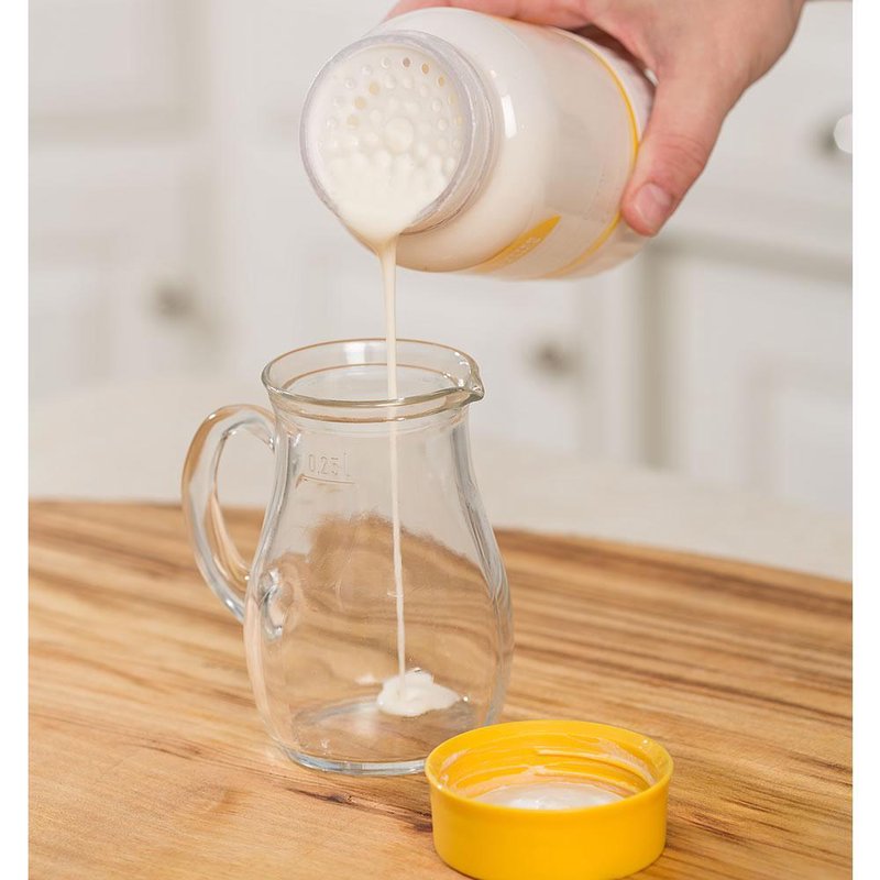 Pouring fresh cream from a handheld Buttercup Butter Maker with yellow lid into a clear glass measuring pitcher on a wooden kitchen counter, featured in Farm, Garden & Tool and Kitchen & Food collections.