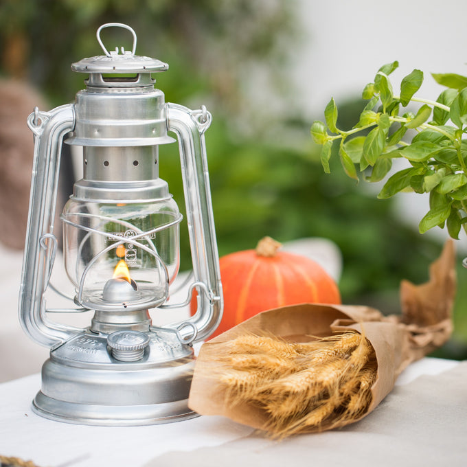 Handcrafted galvanized oil lantern with thermal heat-resistant globe, softly glowing next to a bundle of wheat and autumnal decor, ideal for Lamps & Lighting, Camping, and Emergency Supplies collections.