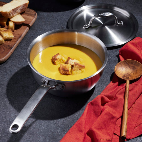 Handmade fully clad stainless steel saucier with lid, filled with soup and croutons, styled on a dark surface with wooden spoon and bread, featured in Kitchen & Food, Cookware, Best Sellers collections.