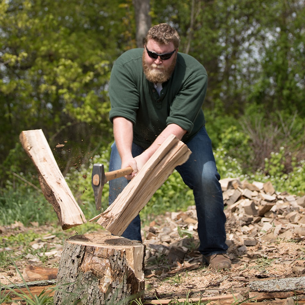 Man vigorously splitting wood with a handcrafted splitting maul outdoors, surrounded by chopped logs, featured in Farm, Garden & Tool, Knives & Axes, and Best Sellers collections.