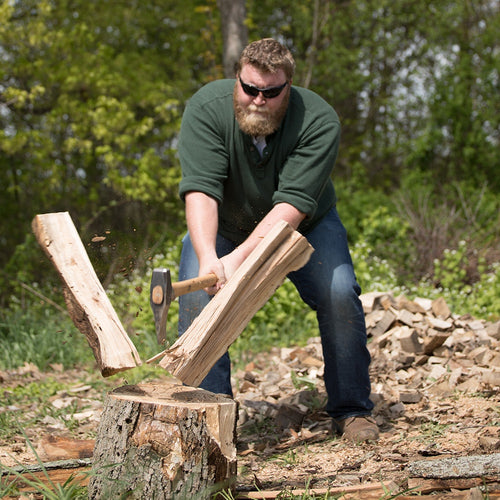 Man vigorously splitting wood with a handcrafted splitting maul outdoors, surrounded by chopped logs, featured in Farm, Garden & Tool, Knives & Axes, and Best Sellers collections.