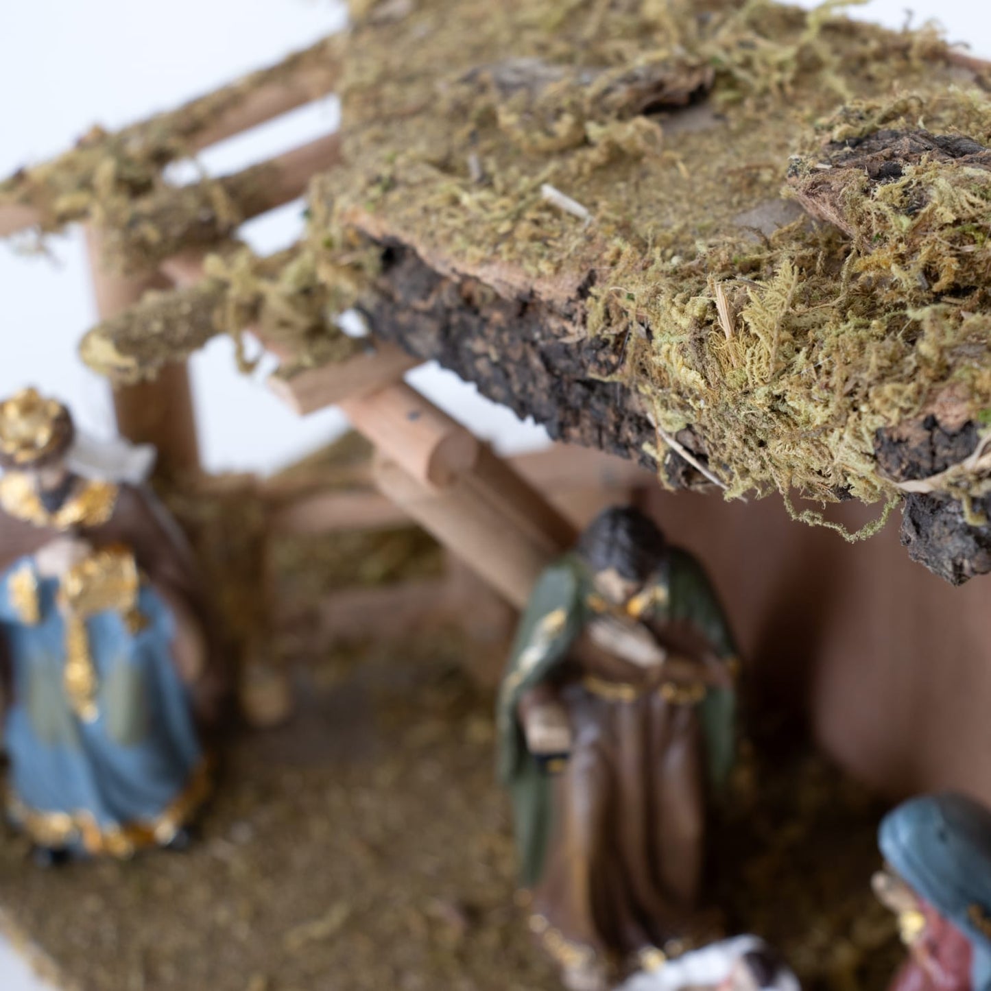 Close-up of a handcrafted resin nativity figurine with golden accents inside a moss-covered wooden stable, styled for Home & Decor, Holiday Decor, Best Sellers, and Promo Eligible collections.