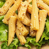 Close-up of pickled baby corn with spices and garlic pieces, resting on a bed of fresh green lettuce, reflecting wholesome Kitchen & Food, Pantry, and USA Made collections.