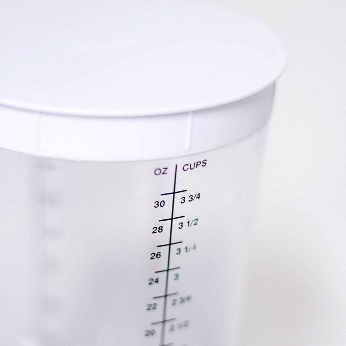 Clear plastic container with black measurement markings in ounces and cups up to 30 oz or 3 3/4 cups, topped with a white fitted lid, part of kitchen and baking helpers collections.