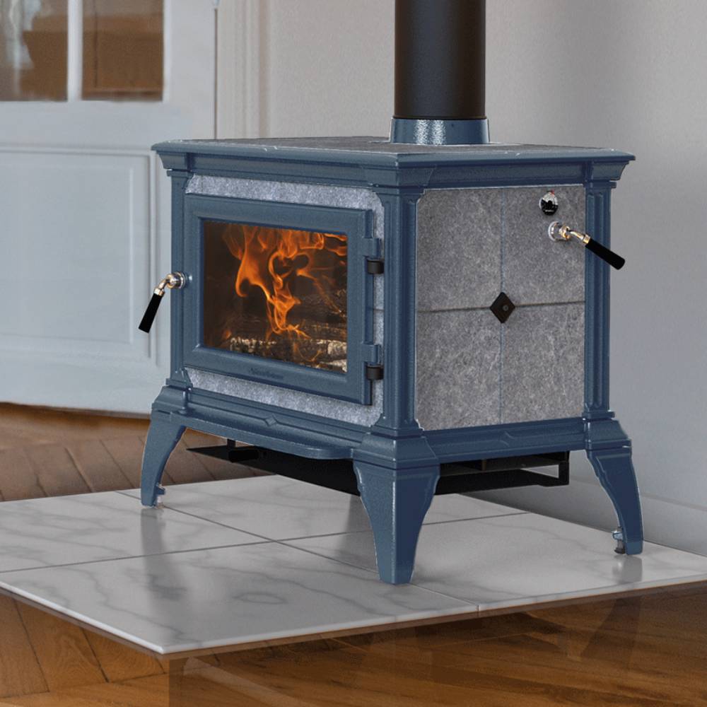 Blue cast iron Hearthstone Castleton 1 TruHybrid wood heat stove with soapstone panels and front glass door showing flame, positioned on white tiled hearth indoors, ideal for Stoves, Heatstoves, Best Sellers, Hearthstone Wood Heatstoves, and All Stoves & Appliances collections.