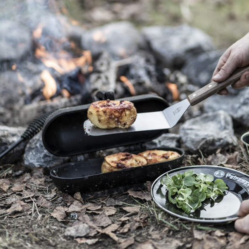 Flexible spatula with a polished stainless steel blade and a smooth wooden handle lifting grilled potato over an open campfire, ideal for Kitchen & Food, Stoves, and Grilling collections.