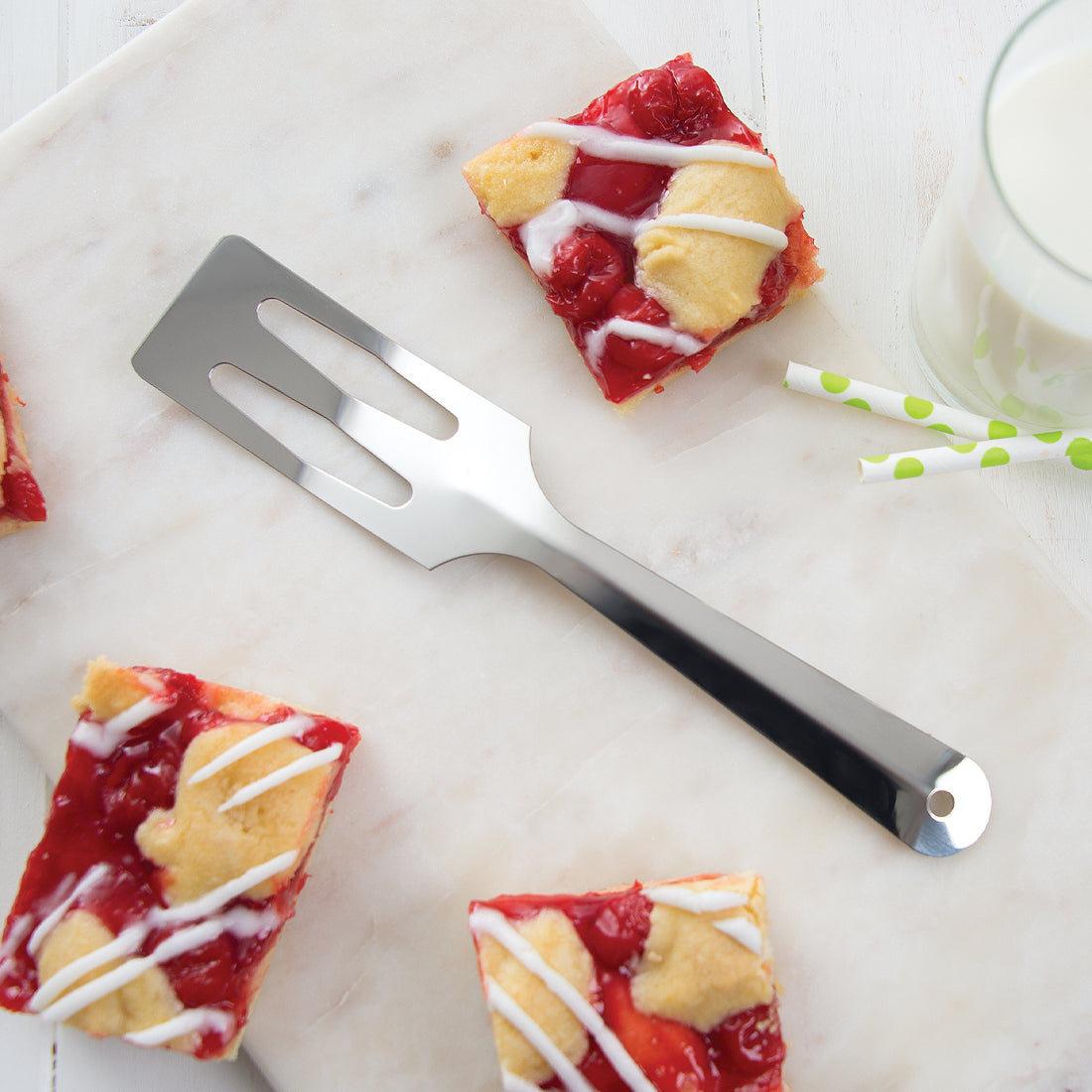 Stainless steel all-purpose kitchen spatula with angled slotted head resting on marble board surrounded by glazed cherry dessert squares, highlighting USA made Kitchen & Food, Storage and Serving, Best Sellers collections.