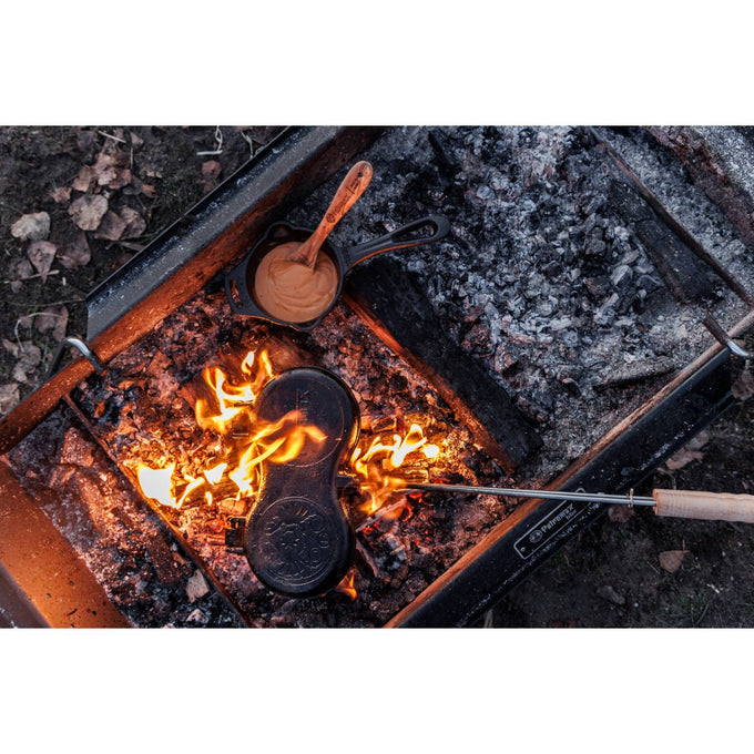 Flame-lit cast iron campfire cooking with a hinged mold roasting bread or pastry, alongside a small bowl of batter and wooden spoon, perfect for outdoor Farm, Garden & Tool and Camping use.