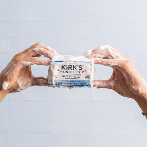 Hands covered in rich foam hold a bar of Original Kirk's Castile Soap with classic packaging, highlighting its gentle formula for Health & Wellness, Grooming, Soaps, and USA Made collections.