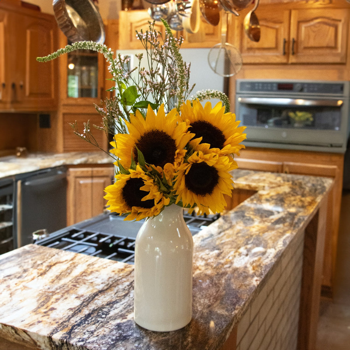 Handcrafted cream-colored stoneware milk bottle filled with fresh sunflowers and greenery, displayed on a granite kitchen island in a rustic home setting, suitable for Home & Decor, Kitchen & Food, and USA Made collections.
