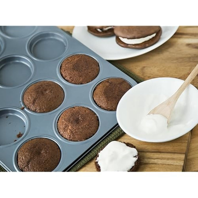 Carbon steel whoopie pie pan with six round baked cakes cooling beside a bowl of white frosting and assembled chocolate whoopie pies on a wooden surface, featured in Kitchen & Food, Cookware, Baking Supplies, and Best Sellers collections.