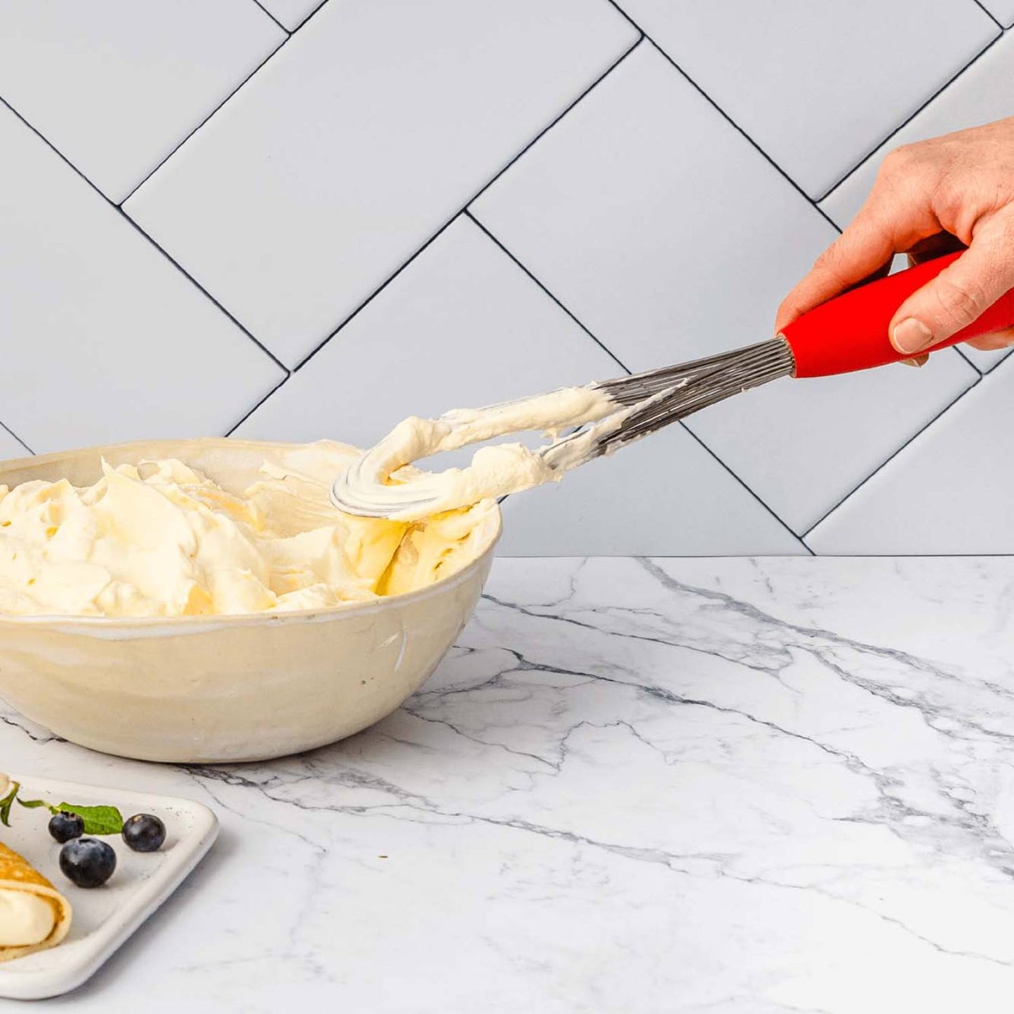 Hand holding a red-handled Flisk 3-in-1 whisk in flat shape, spreading creamy batter in a ceramic bowl, ideal for Kitchen & Food, Kitchen Gadgets, Cooking and Baking Helpers, Best Sellers, Promo Eligible collections.