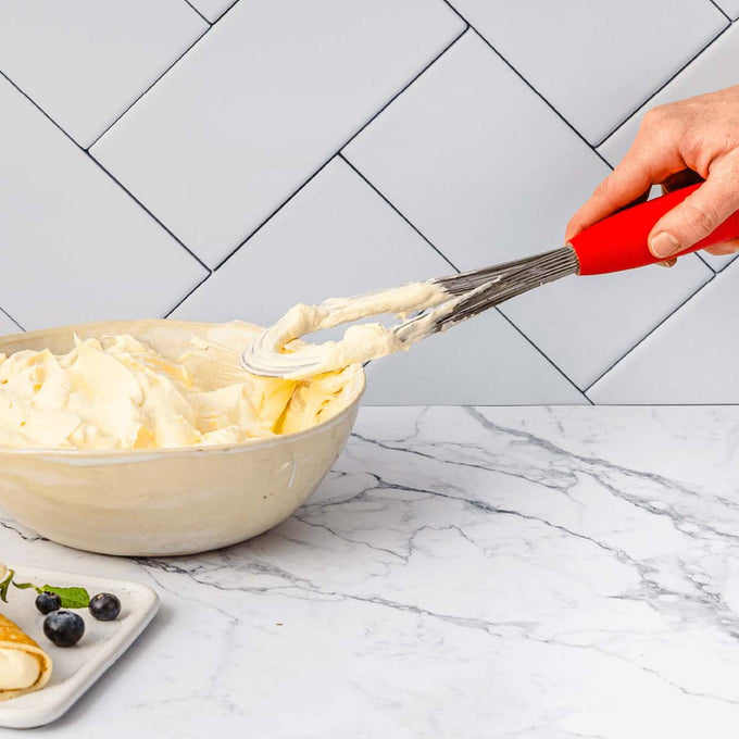 Hand holding a red-handled Flisk 3-in-1 whisk in flat shape, spreading creamy batter in a ceramic bowl, ideal for Kitchen & Food, Kitchen Gadgets, Cooking and Baking Helpers, Best Sellers, Promo Eligible collections.
