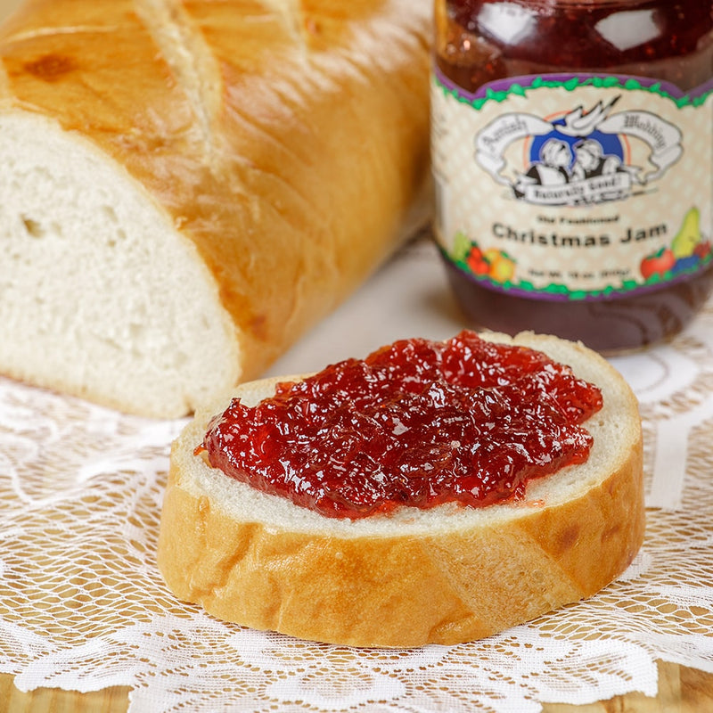 Slice of fresh bread topped with homemade Christmas jam featuring a sweet and tart blend of strawberries and cranberries, with a jar of jam in the background, perfect for Kitchen & Food and Pantry collections.